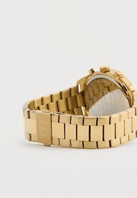 Kuldmetallist link-kellarihm koos klambriga ja osaliselt nähtava kellanäidikuga, millel on kellaoperatsiooni nupud.