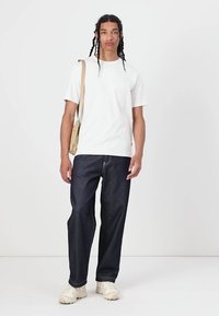 Hvid bomulds t-shirt, mørkeblå løse denim jeans, beige crossbody taske og lyse sneakers. Enkel, afslappet påklædning uden tydelige mønstre.