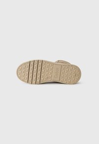 Semelle de chaussure en caoutchouc beige avec des rainures à motifs et un logo en relief ; présente une prise texturée pour la traction et la stabilité.