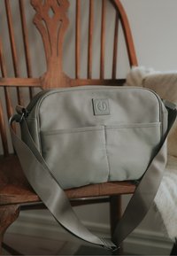 Grå rektangulär axelremsväska i hållbart tyg. Har en frampock, justerbar axelrem och präglad logotyp på framsidan.