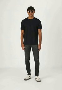 T-shirt preto de manga curta, jeans skinny cinza com detalhes desgastados e ténis brancos com detalhes pretos. Óculos de sol complementam o visual.