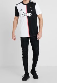 Camisa de fútbol Juventus en blanco y negro con una franja rosa, con la marca Adidas y el logo de Jeep. Combinada con pantalones deportivos negros con franjas blancas.
