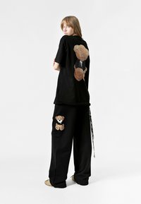 Conjunto de camiseta y pantalones negros que presenta diseños de ositos bordados. La camiseta tiene un gran gráfico de un oso en la espalda, y los pantalones tienen un parche de oso.