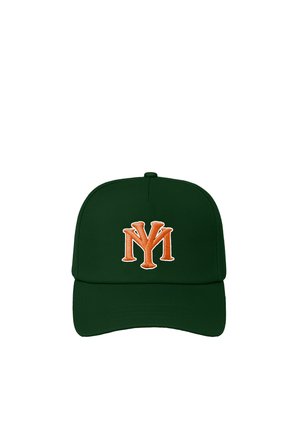 Jeune personne aux longs cheveux foncés portant une casquette vert foncé avec un logo orange, un t-shirt blanc et un pull tricoté rayé vert et crème drapé sur les épaules.