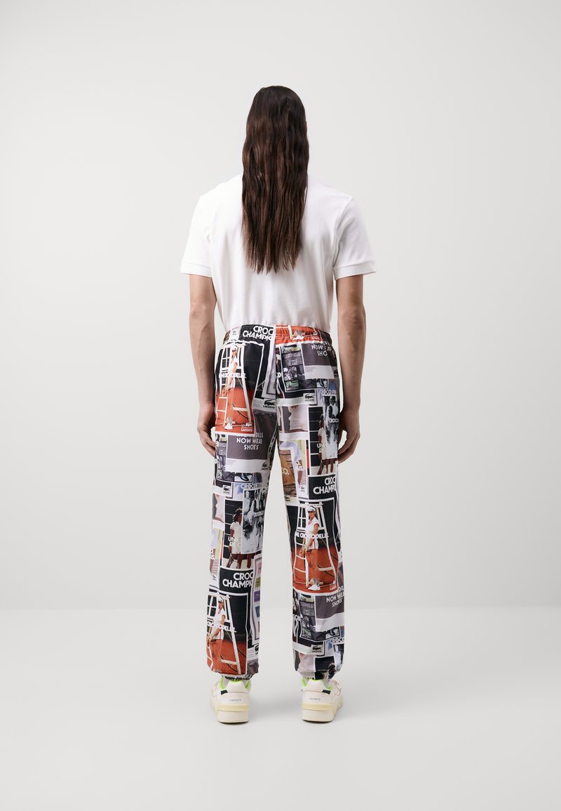 Pantalones multicolores con un patrón de collage que incluye imágenes y texto, cinturilla elástica y tobillos ajustados, combinados con una camiseta blanca sencilla.