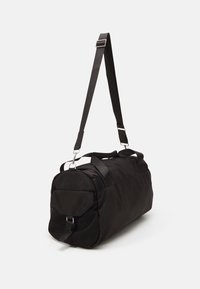 Borsa duffel nera con una texture di tessuto liscia, tracolla removibile, manici doppi e un compartimento con zip a un'estremità.