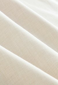 Tissu en toile beige clair avec un motif de tissage en zigzag texturé, présentant des couches pliées et une finition lisse.