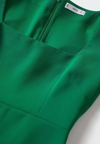 Vihreä mekko neliön muotoisella pääntiellä, valmistettu sileästä kankaasta. Siinä on piilotettu vetskari takana ja minimalistisia suunnittelu-elementtejä.