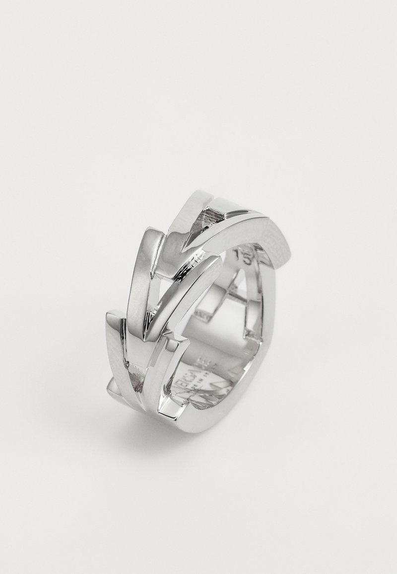 Bague en métal argenté présentant des formes en V entrelacées avec une finition polie, une texture lisse et un design géométrique moderne.