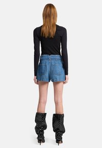 Shorts di denim a vita alta, con tasche posteriori visibili, abbinati a stivali neri a pois e a un top nero a maniche lunghe.