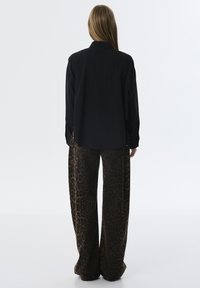 Maglietta nera a maniche lunghe abbinata a pantaloni larghi con stampa leopardata marrone, con una vestibilità rilassata e una texture del tessuto liscia.