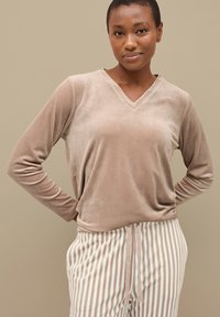 Top de terciopelo beige de manga larga con diseño de escote en V, combinado con pantalones rayados en crema y beige que cuentan con cintura ajustable con cordón.