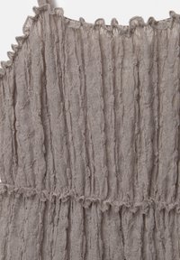 Gros plan sur un tissu en dentelle beige avec des volants texturés verticaux et un détail de bretelle étroite.