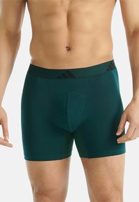 Groene boxershorts gemaakt van gladde stof, met een zwarte tailleband met subtiele branding en een gevormde pouch voor ondersteuning.