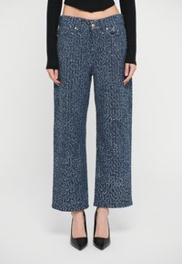 Wide-leg trousers in textured blue fabric, featuring a high waistband with gold hardware accents and a loose fit from hips to ankles.