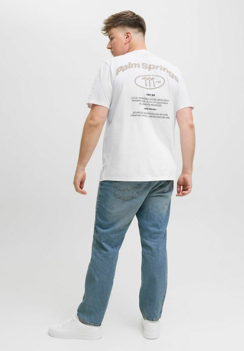 Hvid t-shirt med "Palm Springs" trykt i brunt på ryggen, parret med lyseblå jeans og hvide sneakers. Simpelt, afslappet design.