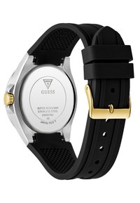 Montre avec bracelet en caoutchouc noir, boîtier en acier inoxydable, éléments en métal doré, accents texturés et un dos étanche marqué avec les détails de la marque.