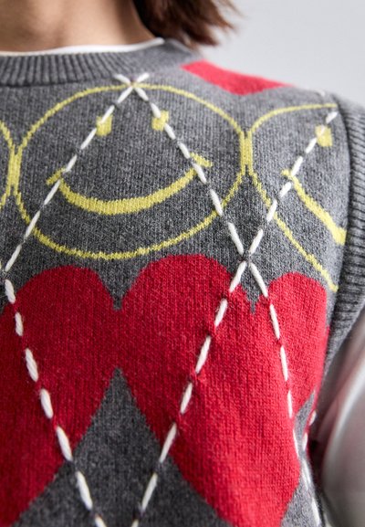 Grauer Strickpullover mit roten Herzen und gelben Smiley-Gesichtern, mit weißen Nähten, die die Muster akzentuieren und einen starken visuellen Kontrast schaffen.