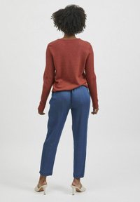Pull en tricot rouge avec un col rond, assorti à un pantalon bleu décontracté et des mules à talons beiges, vu de dos.