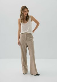 Lekkie, beżowe spodnie w kratę z wysokim stanem i szerokimi nogawkami, w połączeniu z białym, bezrękawnikowym, luźnym topem. Czarne, szpiczaste buty.