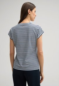 Marineblauwe en witte gestreepte T-shirt met korte mouwen, ronde hals en een metalen accent op de rug. Zacht materiaal en een relaxte pasvorm.