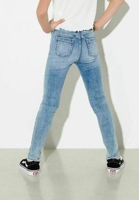 Smal ljusblå jeans med fransad midja, tre fickor och subtil blekning på låren, i kombination med svarta och vita sneakers.