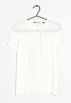 Biała bluzka z krótkim rękawem, okrągłym dekoltem i plisami z przodu, wisząca na czarnym wieszaku na białym tle.