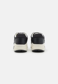Zapatillas negras con parte superior sintética lisa, mediado crema y suela de goma texturizada. Incluye un cuello acolchado y un diseño minimalista.