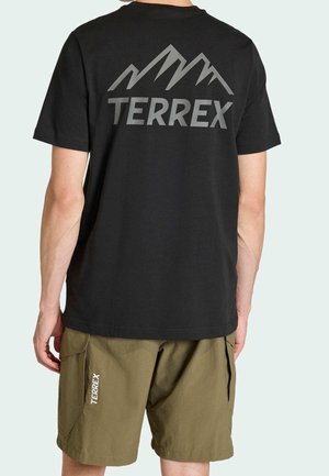 Mężczyzna w czarnej koszulce Terrex z logo góry na plecach i oliwkowych szortach Terrex z bocznymi kieszeniami.