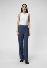 Un haut sans manches blanc associé à un pantalon large taille haute bleu marine. Tissu lisse avec un léger éclat, complété par des chaussures noires.