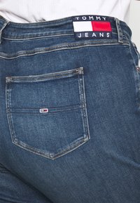 Mörkblå jeans i denim med en bakficka som har en röd, vit och blå logotypmärke. Raka ben, synliga sömmar och minimalistisk design.