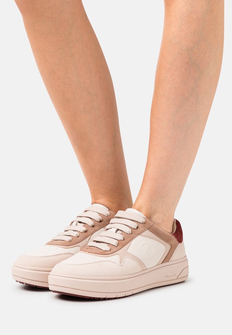 Cremefarbene und beige Sneakers mit strukturierten Wildlederakzenten und kontrastierendem roten Absatz. Sie verfügen über flache Schnürsenkel und eine dicke, gepolsterte Sohle.
