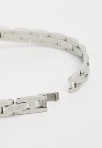 Pulsera de acero inoxidable con eslabones ovalados, que cuenta con un cierre grabado con "GUESS". Acabado pulido con una textura suave.