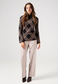 Top a maniche lunghe nero con motivo rosa e texture a coste, abbinato a pantaloni beige chiari a gamba larga e stivali lucidi marroni a punta.