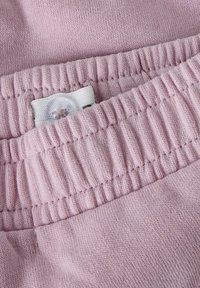 Lichtroze stof met een zachte textuur, voorzien van een rekbare tailleband en een wit label met een rond knoopdetail.