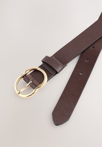 Ceinture en cuir marron avec une boucle arrondie en métal doré, texture lisse, et plusieurs trous de réglage tout le long de la sangle.
