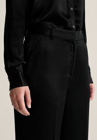 Svart satin skjorta med knäppning fram och långa ärmar, parat med matchande högmidjade byxor med sidofickor och en slät yta.
