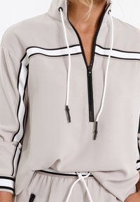 Hellgrauer Kapuzenpullover mit Reißverschluss in Schwarz-Weiß-Streifen, mit Kordelzug und weicher Textur. Hat ein Viertel-Reißverschluss-Design und eine lockere Passform.