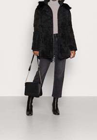 Svart puffjacka med blommönster och faux päls på huven, bärs över en grå polotröja, tillsammans med svarta jeans och svarta klackstövlar.