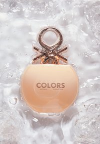 Flacon de parfum rond couleur pêche avec un bouchon métallique en boucle flottant dans de l'eau claire avec des bulles.