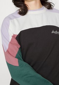 Felpa a blocchi di colore con pannelli neri, bianchi, lavanda, rosa e verdi. Texture morbida, scollo rotondo e dettaglio del logo ricamato.