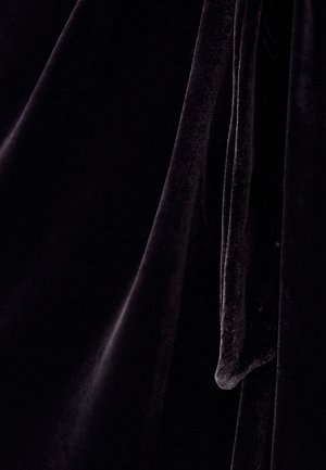 Melna samta auduma ar mīkstu, gludu tekstūru, kas izceļas ar plūstošām drānām un vieglu spīdumu. Materiāls izskatās bagāts un grezns.