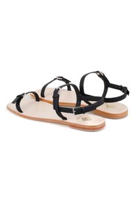 Zwarte leren sandalen hebben verstelbare bandjes, een minimalistisch ontwerp en een vlakke tan kleurige zool met subtiele textuur en laagprofil hardware.