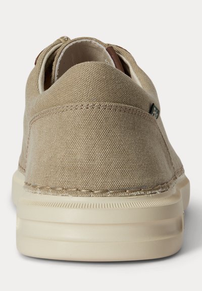 Casual superga iz bež platna, videti od zadaj z vidnimi šivi in debelim, rahlo belim gumijastim podplatom.