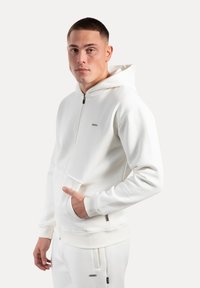 Hoodie bianco con zip frontale, cappuccio regolabile, polsini a coste e tasche laterali; realizzato in morbido tessuto testurizzato.