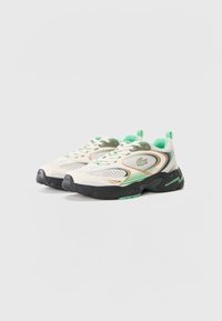 Lacoste sneakers featuring a cream mesh upper with green and brown accents, black rubber sole, and a green logo on the side.