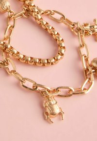 Guld kædearmbånd med en tekstureret linksdesign, prydet med en bille charme og en udsmykket sfærisk accent. Designet for at skabe en dristig effekt.