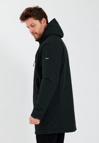 Zwarte capuchonjack met een gladde, matte afwerking. Voorzien van een ritszak aan de zijkant, verstelbare koorden en een ontspannen pasvorm.