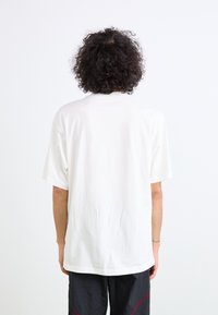 T-shirt blanc en coton avec des manches courtes, une coupe décontractée et un col rond, présentant une texture lisse et unie sans logos ni motifs visibles.