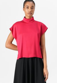 Red, high-neck t-shirt with short sleeves, made of smooth fabric, featuring a loose, cropped fit, paired with a black, flowing skirt.